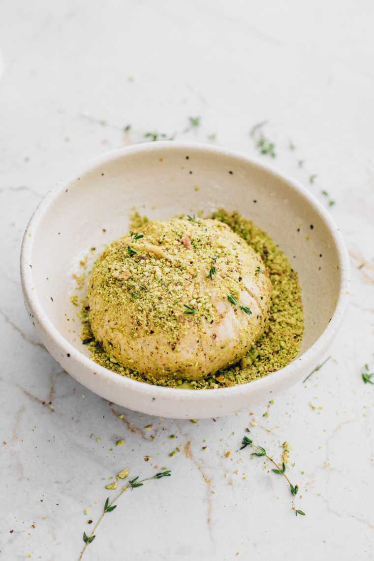 white bowl with crushed pistachios and herbs which are used to roll an almond cheese ball in