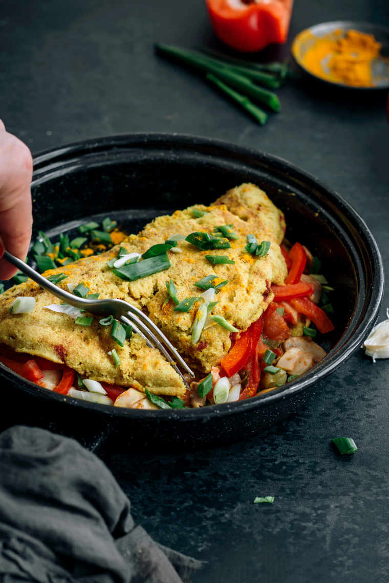 black plate on a table with a folded vegan chickpea omelette in which a fork is being pierced