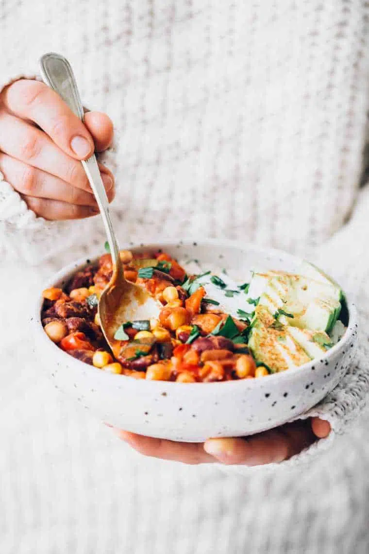 woman holding bowl of vegan bean chili and dipping spoon into the food