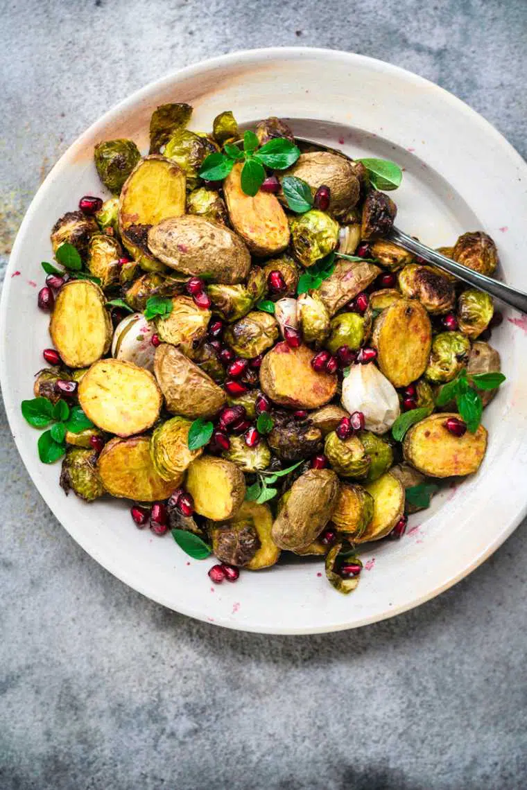 white plate with roasted potatoes, brussels sprouts and pomegranate seeds