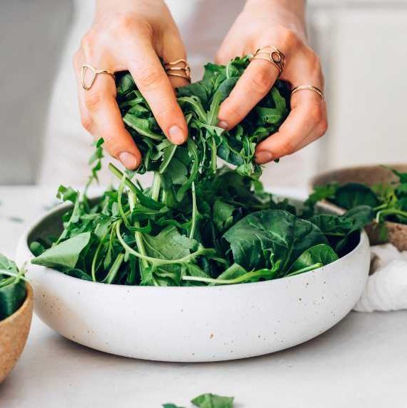 two hands holding fresh baby spinach of a large white bowl