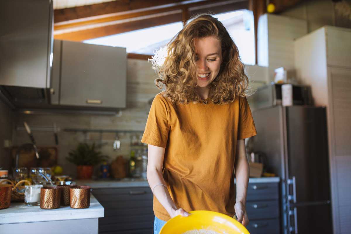 woman in yellow short laughing in her kitchen whole cooking