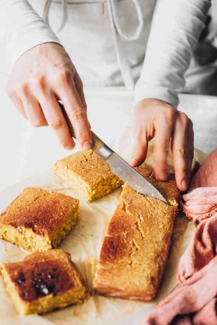 Woman with white apron cutting freshly baked cornbread into six equal squares