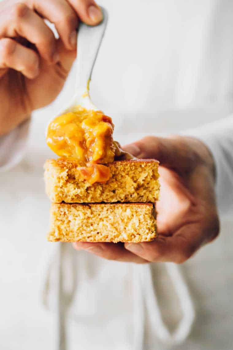 Close up shot with shallow focus of woman holding two pieces of vegan cornbread and spreading a spoonful of mango chutney on top