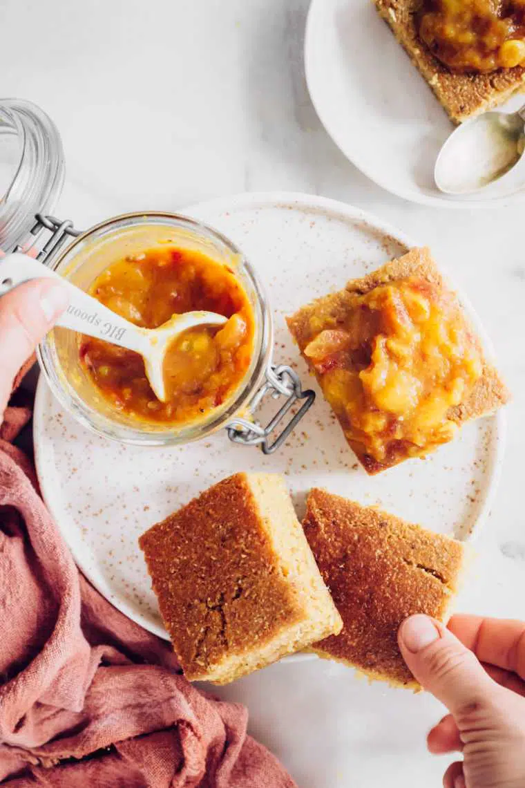 glass of sugar free chutney next to some pieces of freshly baked vegan cornbread on a plate