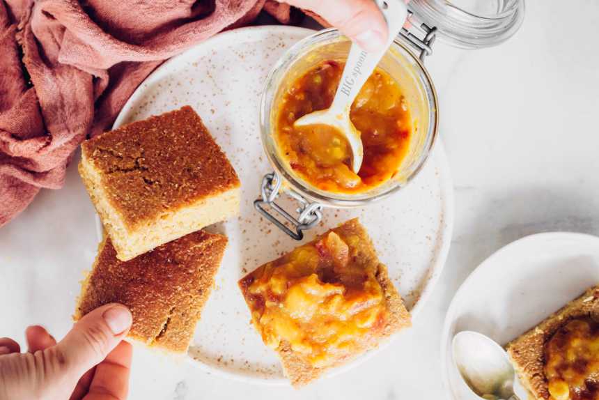 Top view of vegan cornbread squares on plate next to a glass jar of mango chutney