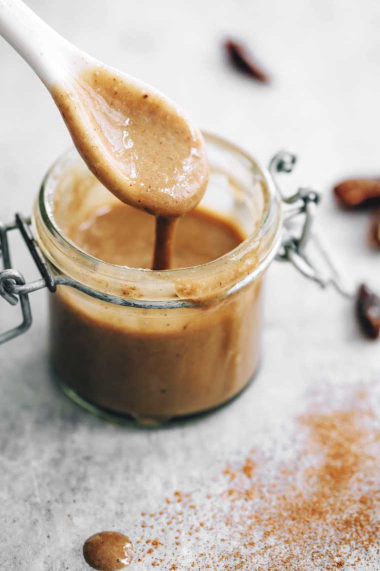 small glass jar with vegan caramel sauce dripping from a spoon