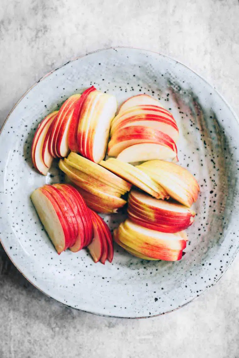 white speckled bowl on a table with some thinly sliced apple