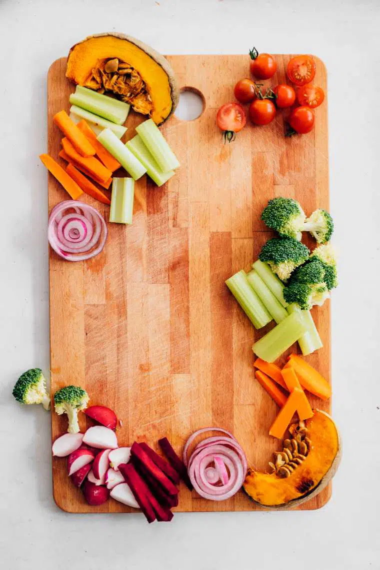 wooden appetizer platter with colorful veggies such as roasted pumpkin, fresh tomatoes, broccoli and carrot sticks