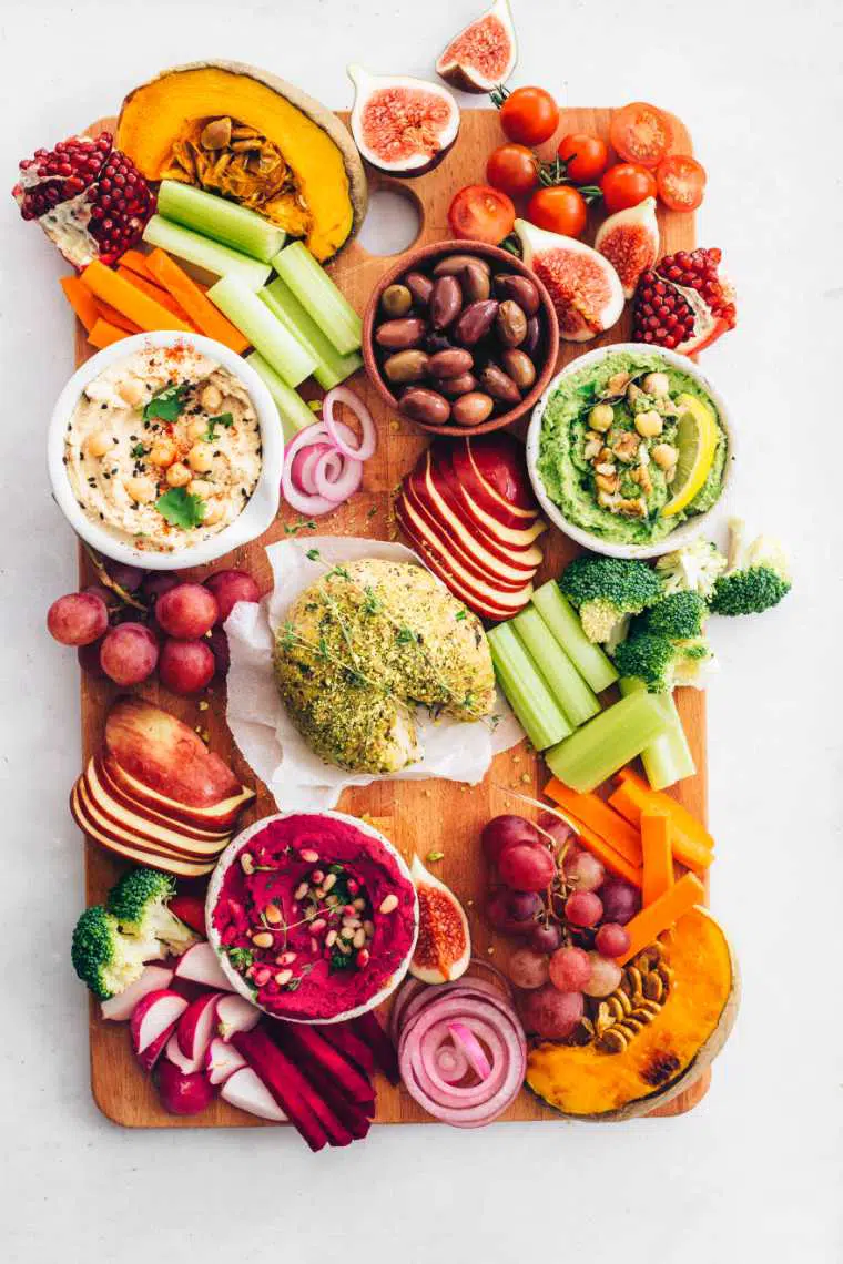wooden board with colorful fruits and vegetables, hummus and vegan cheese