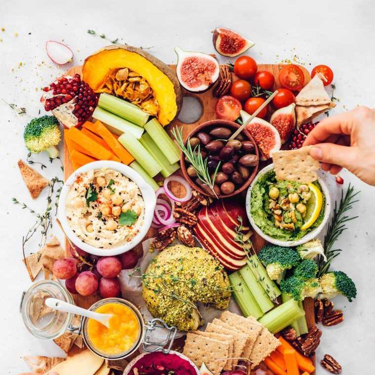 two hands reaching for parts of a colorful vegan fall appetizer platter with hummus and cheese