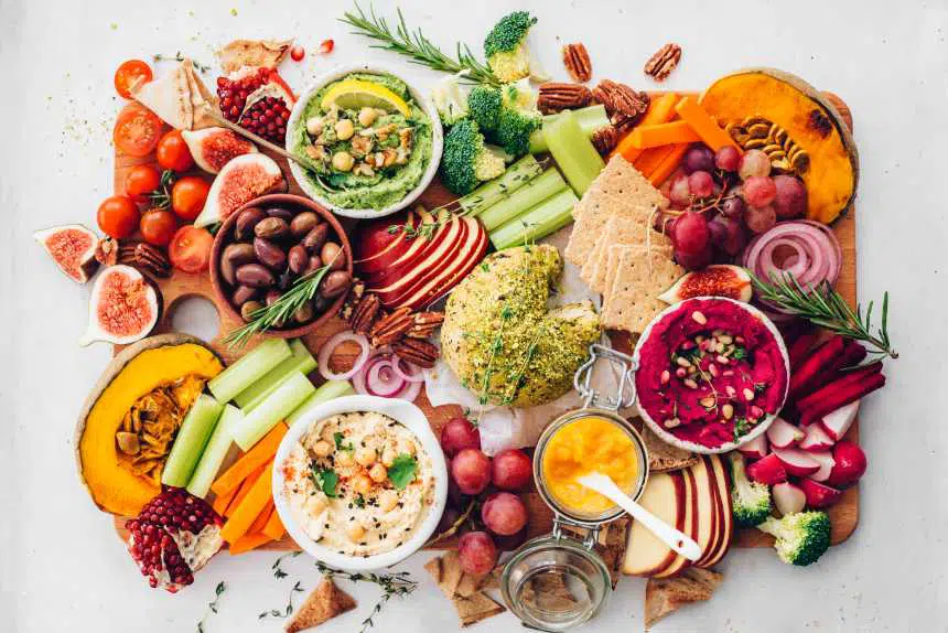colorful vegan appetizer platter with crackers, fall produce, 3 types of hummus and nut cheese
