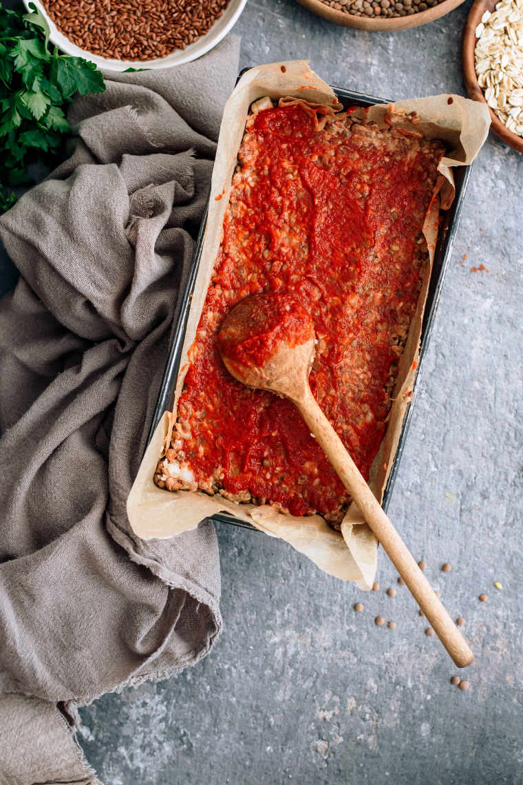 baking dish with parchment and vegan lentil loaf with red topping and a wooden spoon