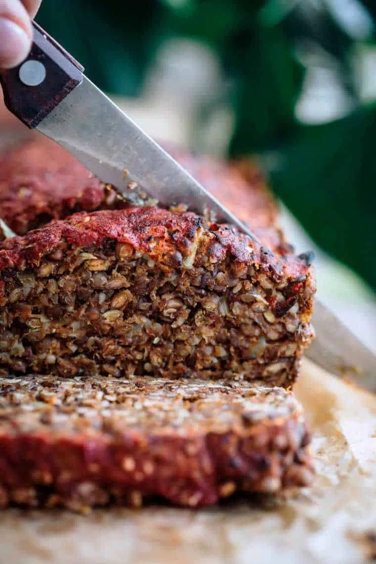 hand holding a knife and slicing vegan meat loaf on a chopping board