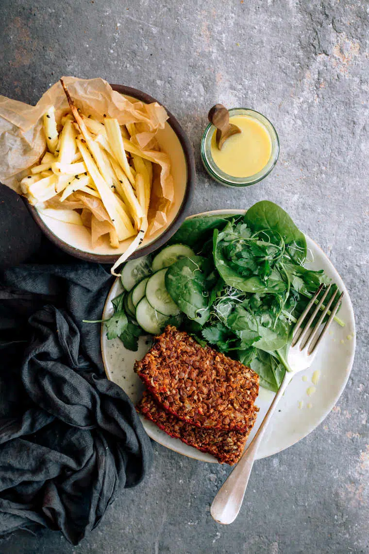 white plate with green salad, two slices of lentil loaf and a fork next to some parsnip fries