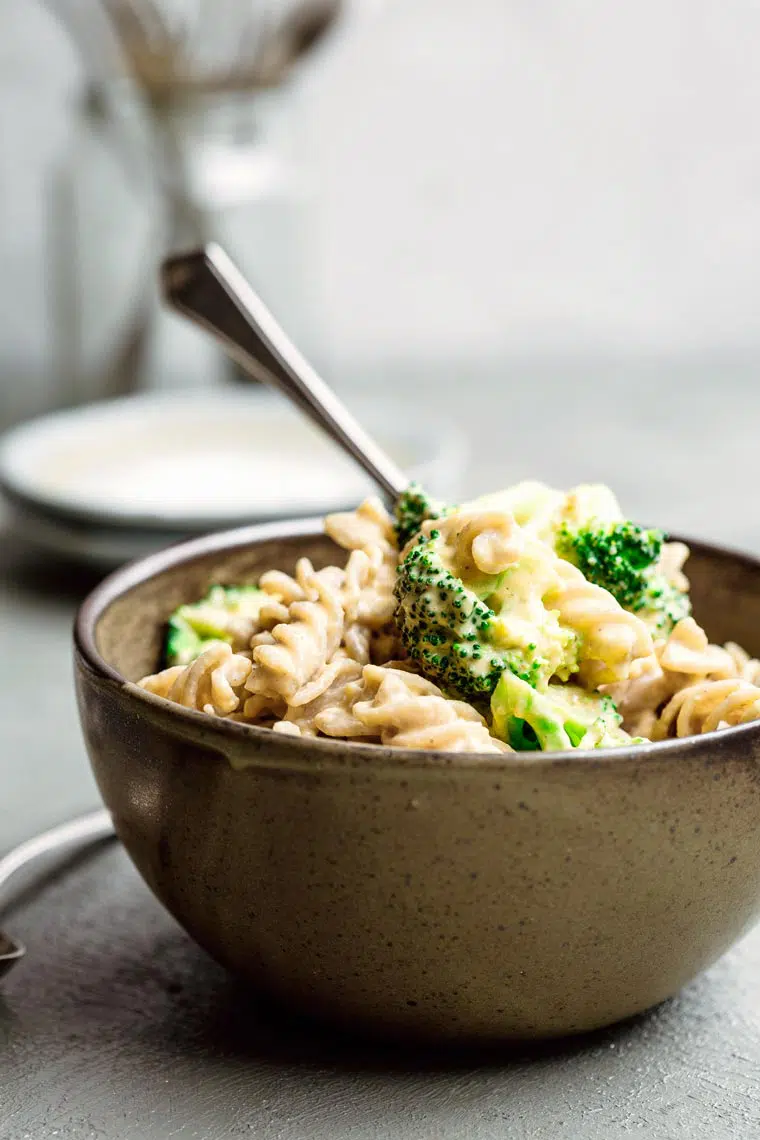 close-up of a bowl with whole food plant-based mac and cheese with broccoli and a spoon