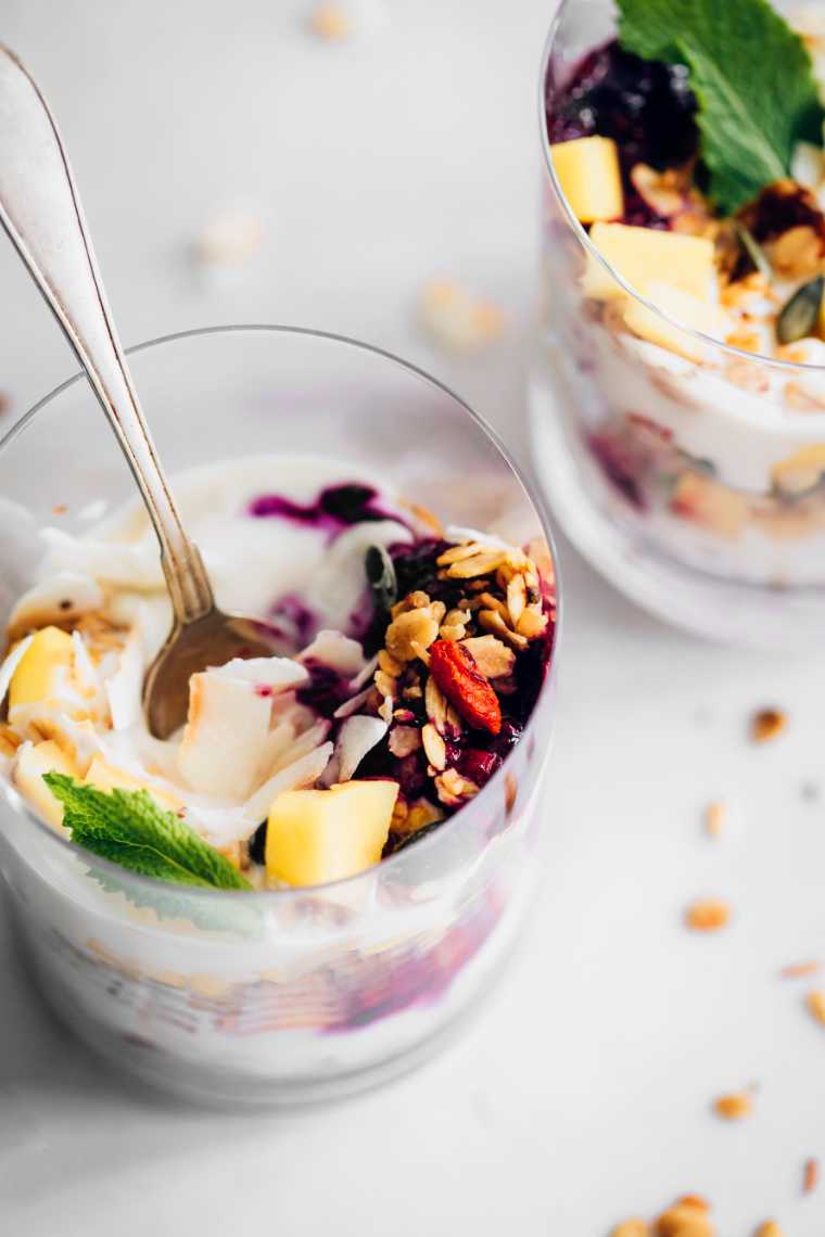 white table with two glass jars filled with almond yogurt, mango, granola and blueberries