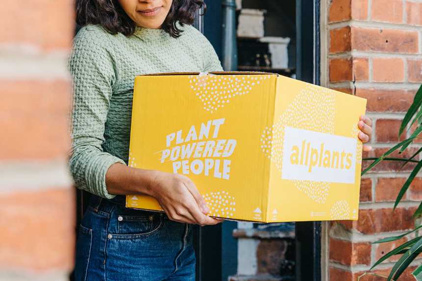 woman holding a yellow vegan meal delivery box from allplants in her hands
