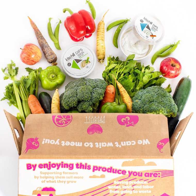 large cardboard box by imperfect produce filled to the brim with different fresh veggies and vegan dips