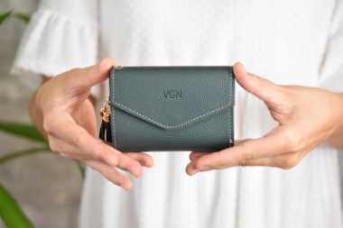 woman in white dress holding a small vegan wallet with the letters "vgn"