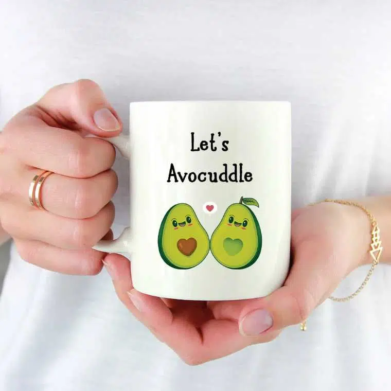 woman holding a white mug with two avocado halves and the words "let's avocuddle"