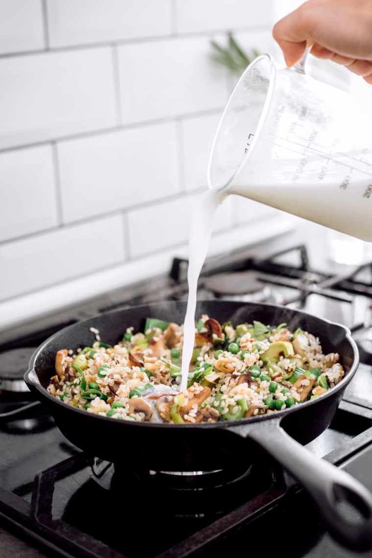 pouring plant-based milk into black pan with vegan mushroom and pea risotto