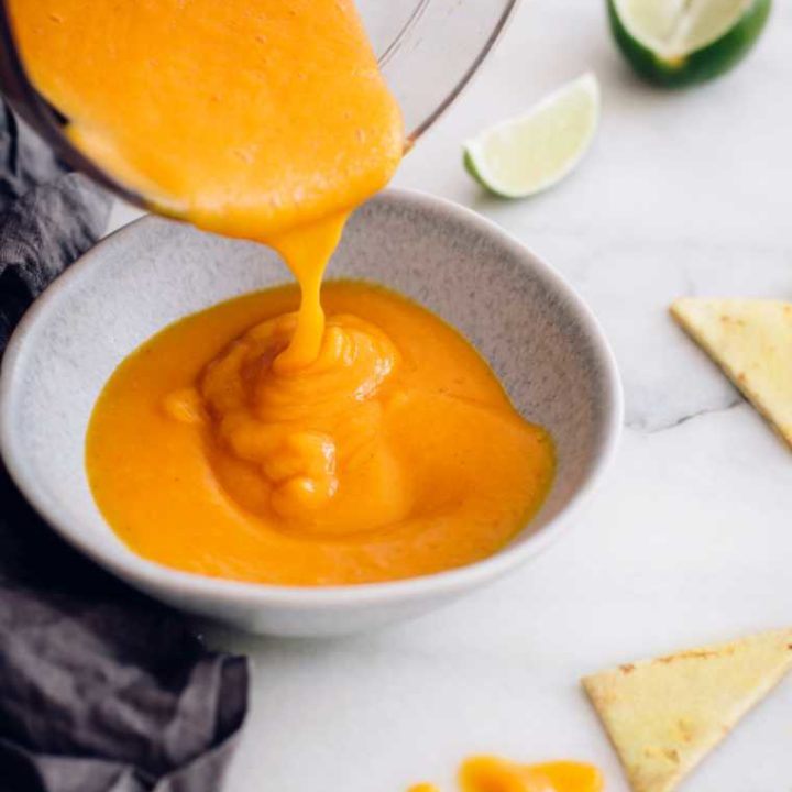 blender jar pouring plant-based low fat nacho cheese sauce into a small bowl