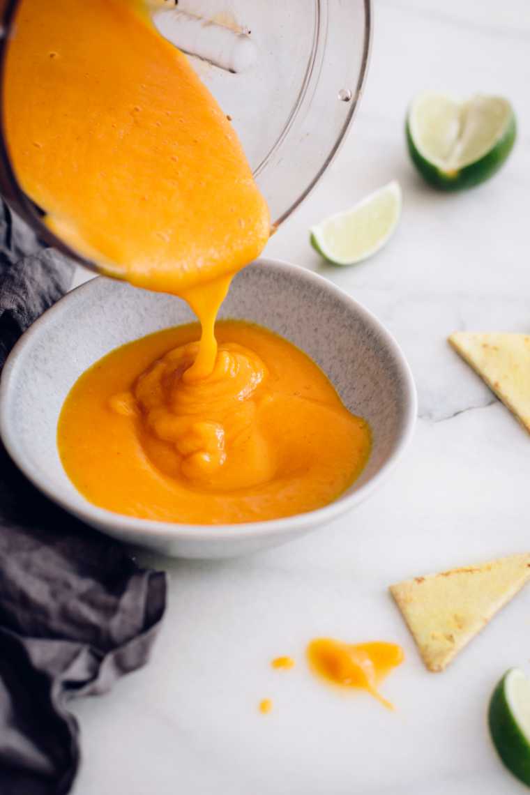 blender jar pouring plant-based low fat queso into a small bowl