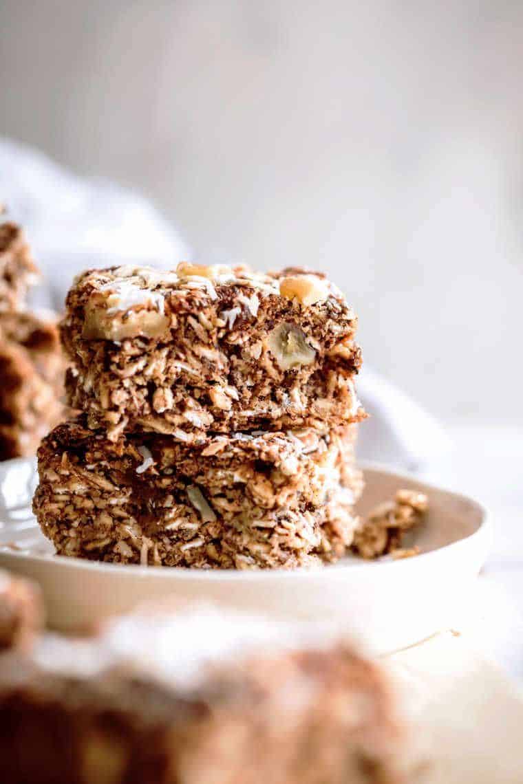 two vegan oat bars on top of each other on a white plate standing on a table