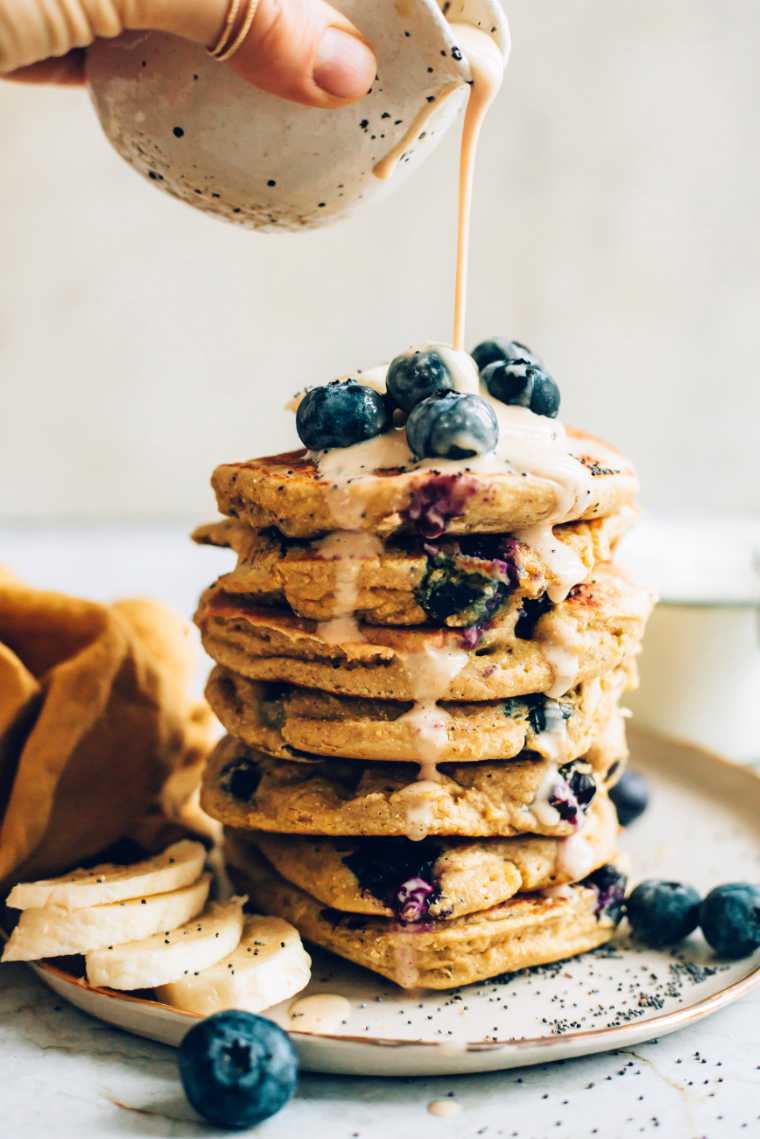 pouring sauce over a stack of vegan blueberry pancakes