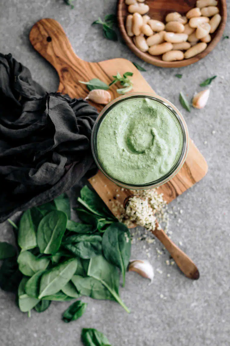 top view of a table with white beans, spinach, garlic, hemp seeds and homemade vegan sauce