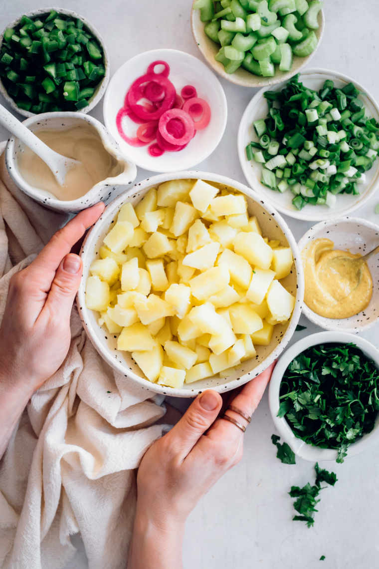 different sized white bowls with ingredients such as cooked potatoes, radishes, green onion, mustard and cashew mayo for a vegan potato salad
