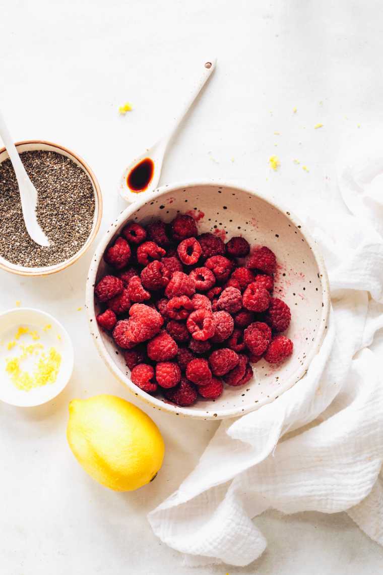 white bowl with raspberries next to a lemon, vanilla and chia seeds