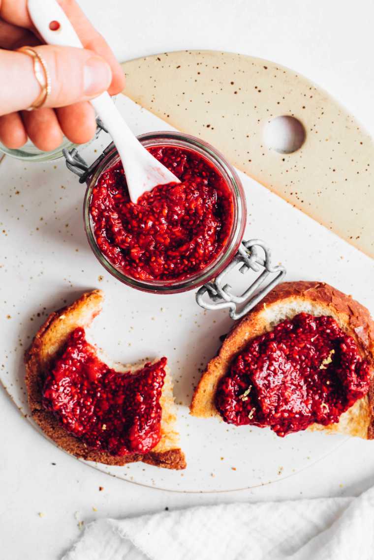 white chopping board with two slices of bread spread with sugar-free berry chia jam next to a glass jar