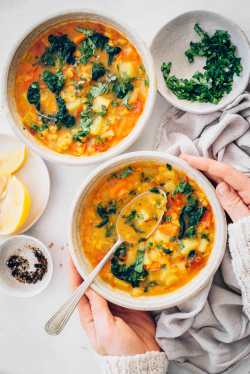 Two bowls of vegan red lentil soups with female hands holding one of the bowls