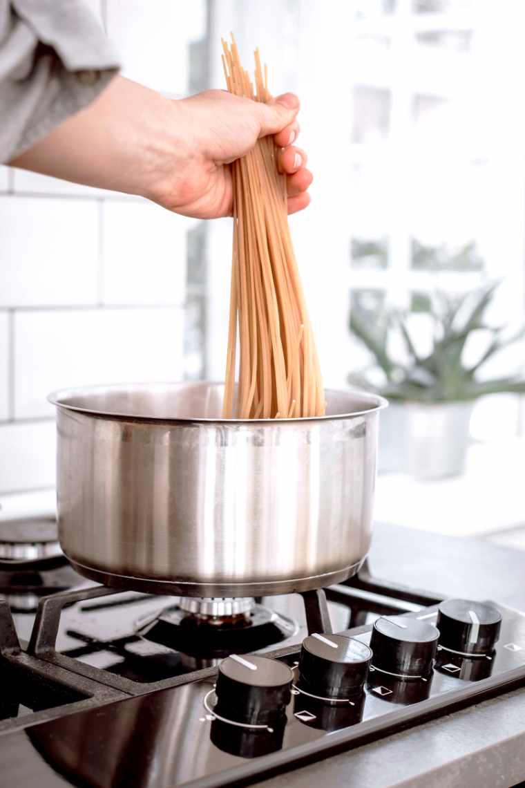 woman holding spaghetti in one hand and placing it into a pot with boiling water