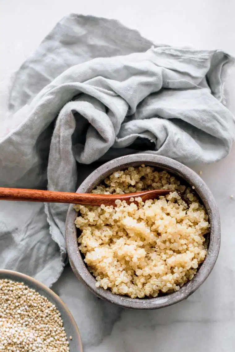 bowl of cooked quinoa and a wooden spoon next to a linen towel