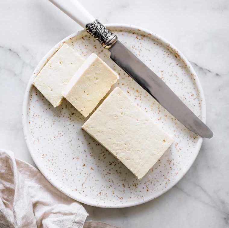 white plate with a block of plain tofu next to a knife