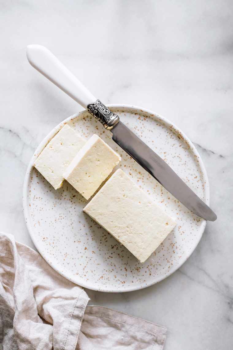 white plate with a block of plain tofu next to a knife