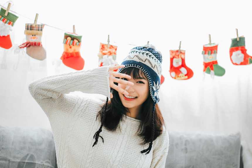 woman with cozy sweater sitting on a sofa in front of several Christmas stockings and smiling