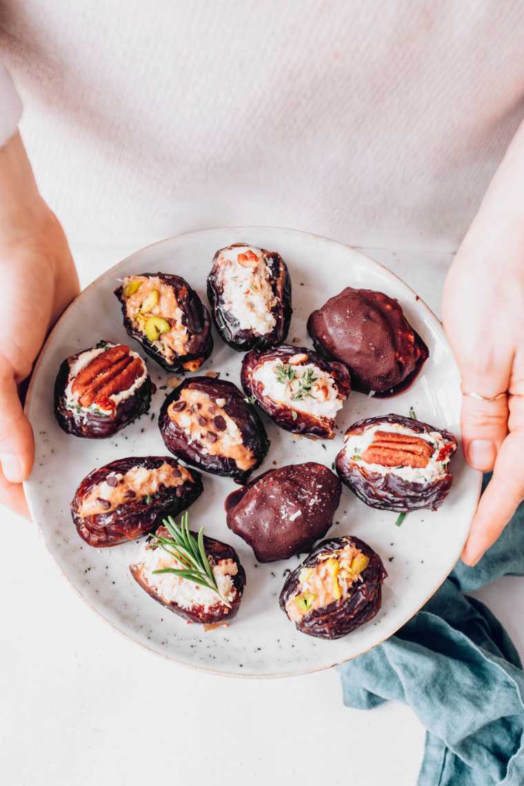 woman holding a white plate with several different kinds of vegan stuffed dates