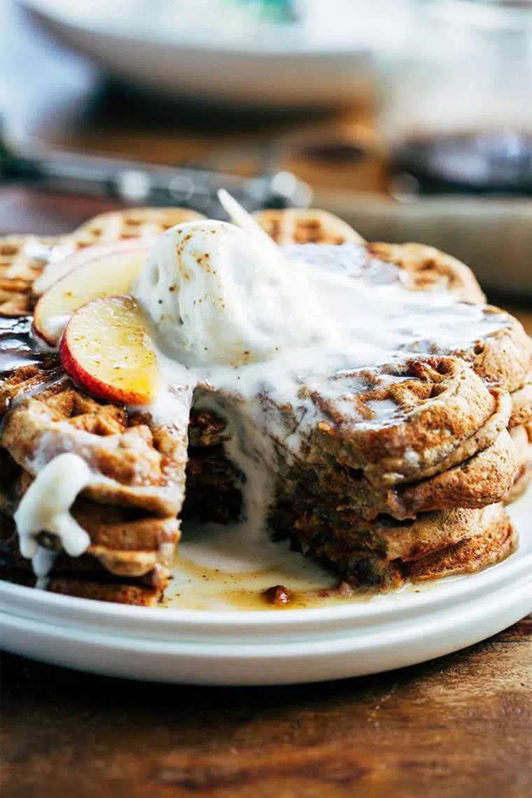 white plate with three apple pie waffles stacked on top of each other with some melting vegan vanilla ice cream on top