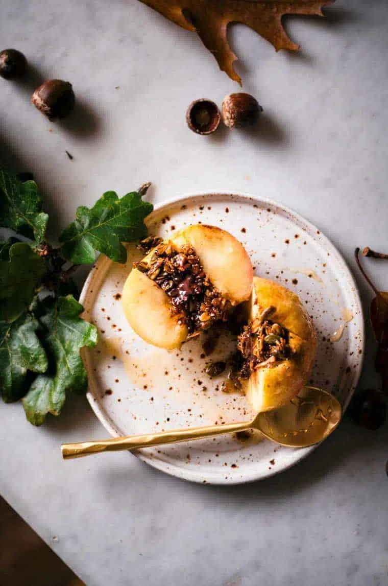 Baked Apples Stuffed with Granola and Dark Chocolate on a white plate next to a golden spoon