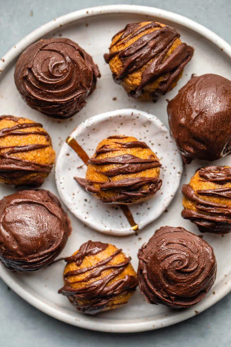 nine small round vegan pumpkin truffles covered more or less in chocolate on a white plate