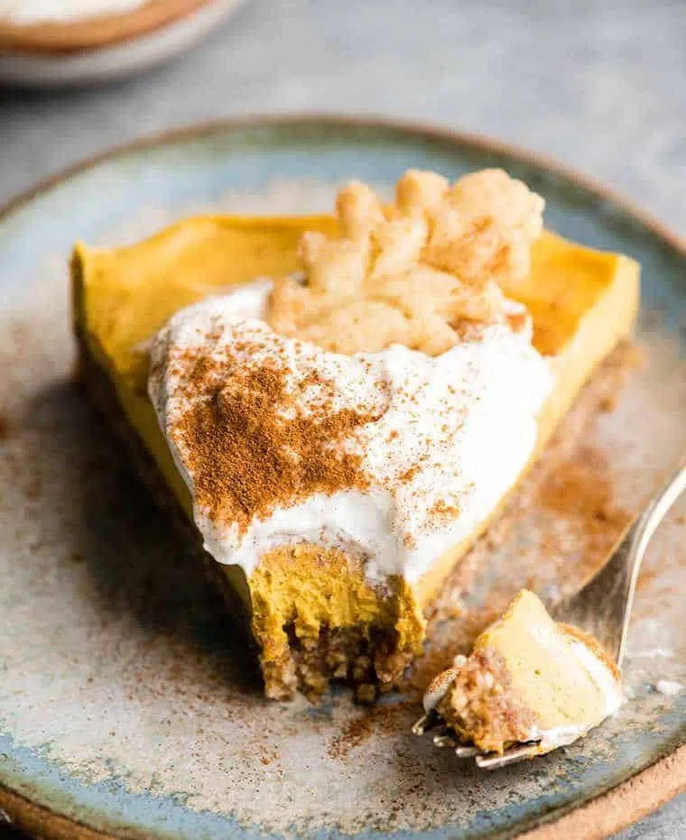 one piece of no bake vegan pumpkin cheesecake with coconut whipped cream and a cooke on a blue plate for a healthy thanksgiving dessert