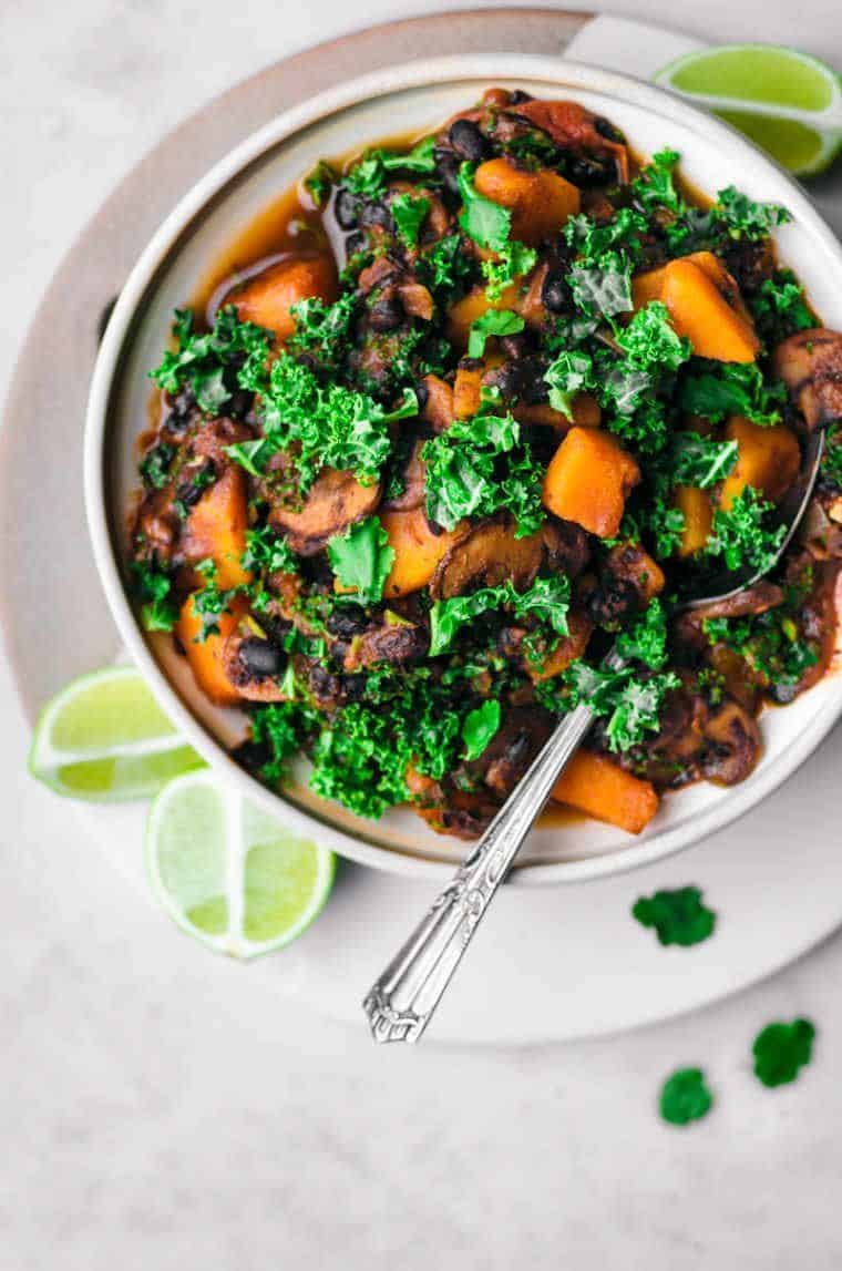 white bowl with a spoon and a black bean pumpkin chili with kale