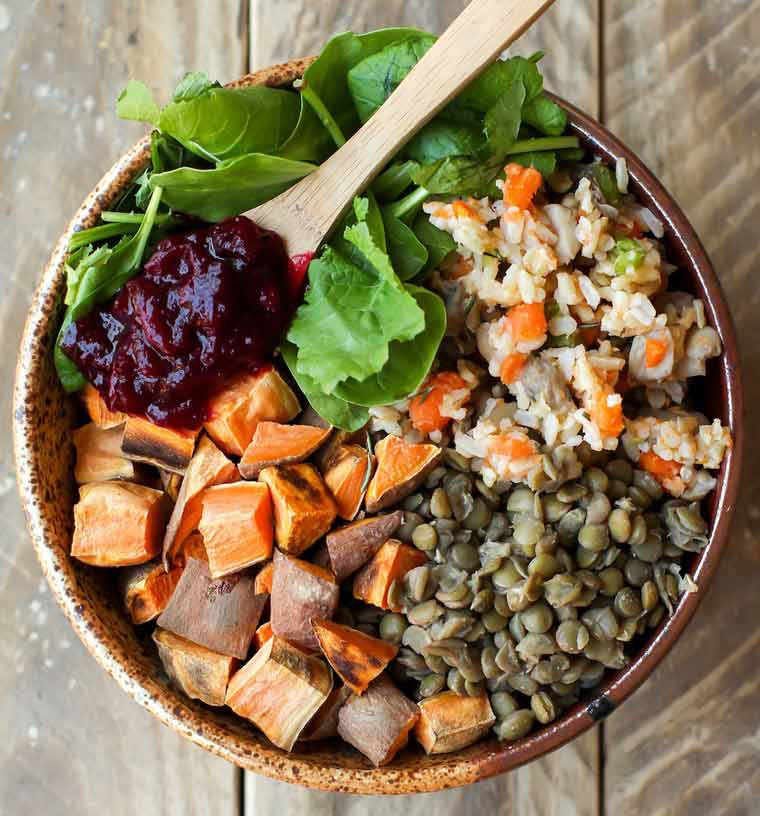 brown bowl on wooden surface filled with baked sweet potato, cooked green lentils, rice, leafy greens and cranberry sauce for a quick vegan thanksgiving