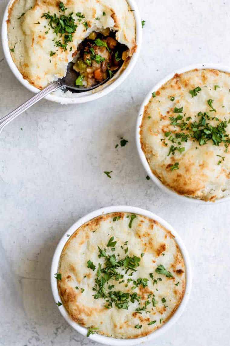 three small white bowls with vegan lentil shepherds pies with a vegetable filling