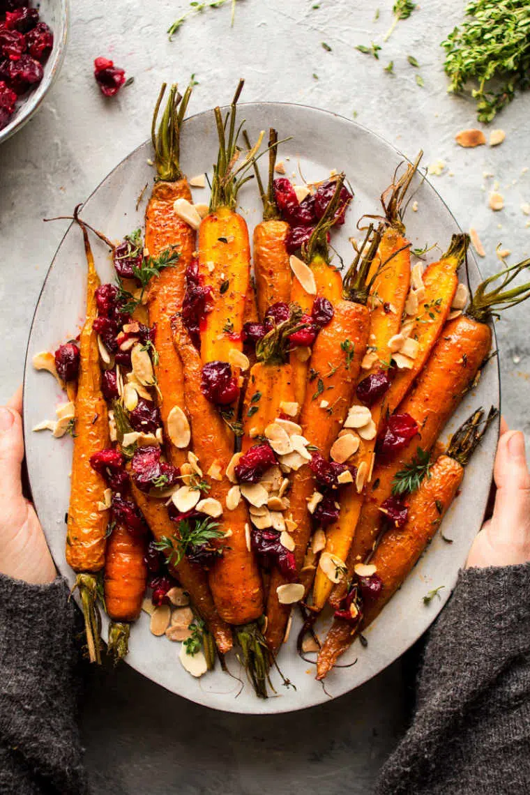 white plate of roasted carrots with cranberries and almonds on a white table