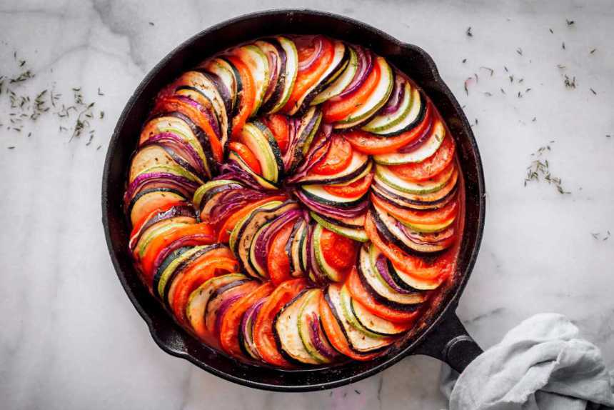 black baking dish with layered summer vegetables on tomato sauce